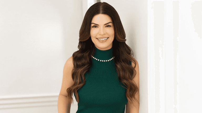 Smiling woman in a green dress with long, wavy hair standing by a wall