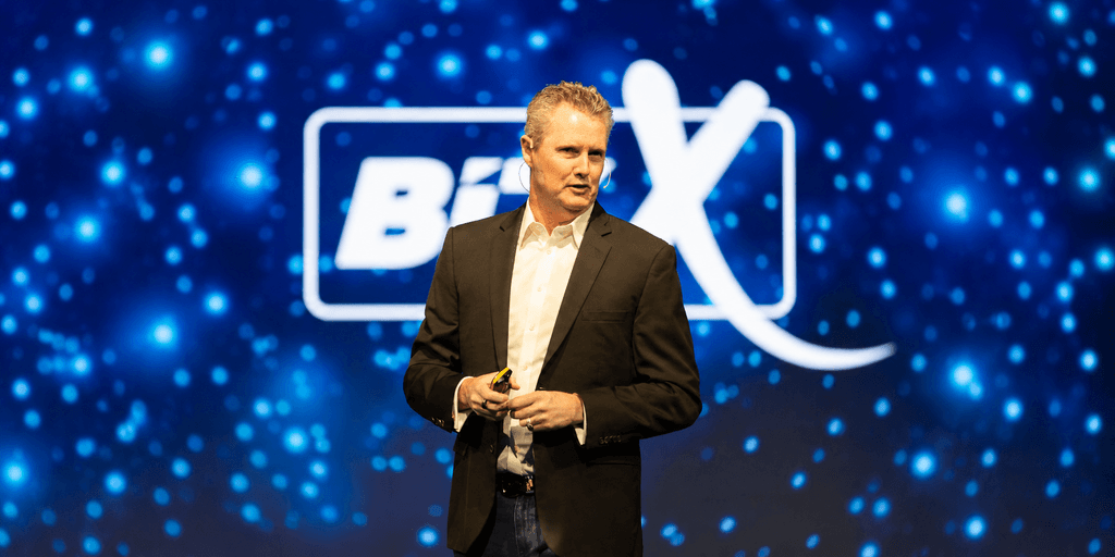 A speaker presenting on stage with a colorful background at a conference event