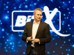A speaker presenting on stage with a colorful background at a conference event