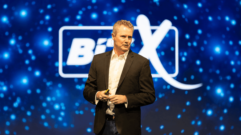 A speaker presenting on stage with a colorful background at a conference event