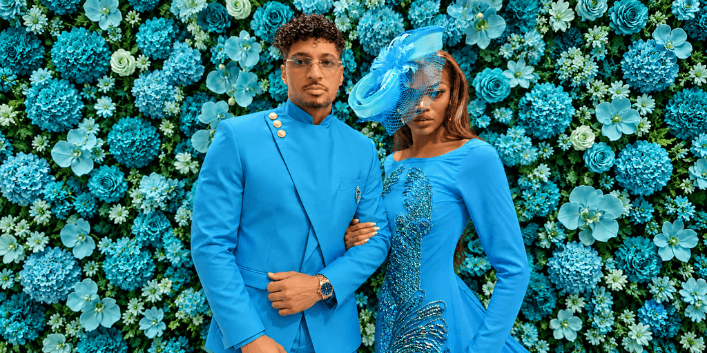 A couple poses together in matching blue outfits against a vibrant floral backdrop