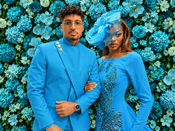 A couple poses together in matching blue outfits against a vibrant floral backdrop