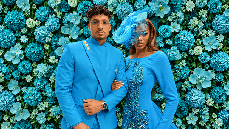A couple poses together in matching blue outfits against a vibrant floral backdrop