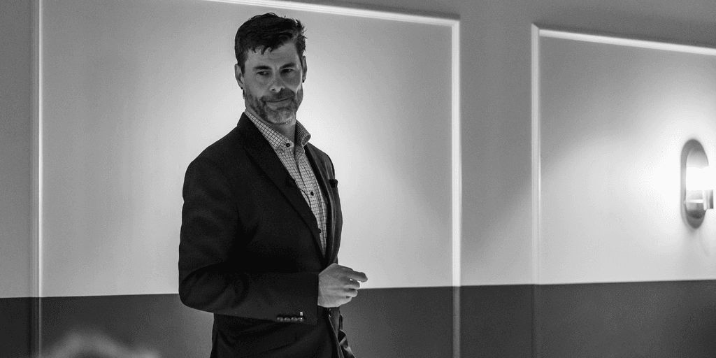 A man presenting on stage in a dimly lit conference room