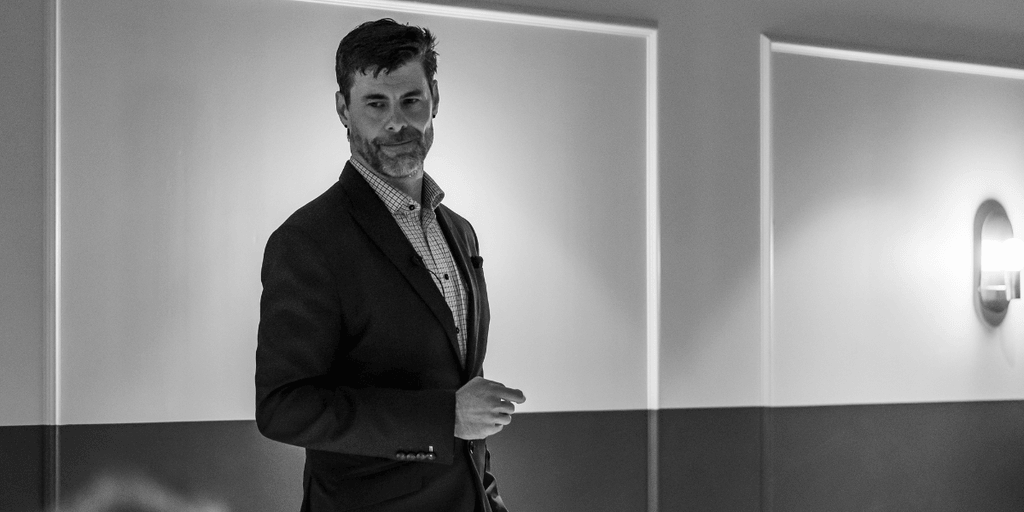 A man presenting on stage in a dimly lit conference room