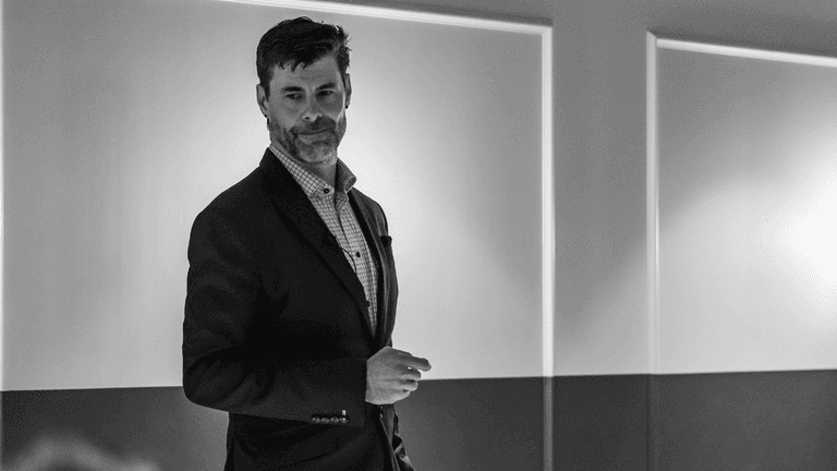 A man presenting on stage in a dimly lit conference room