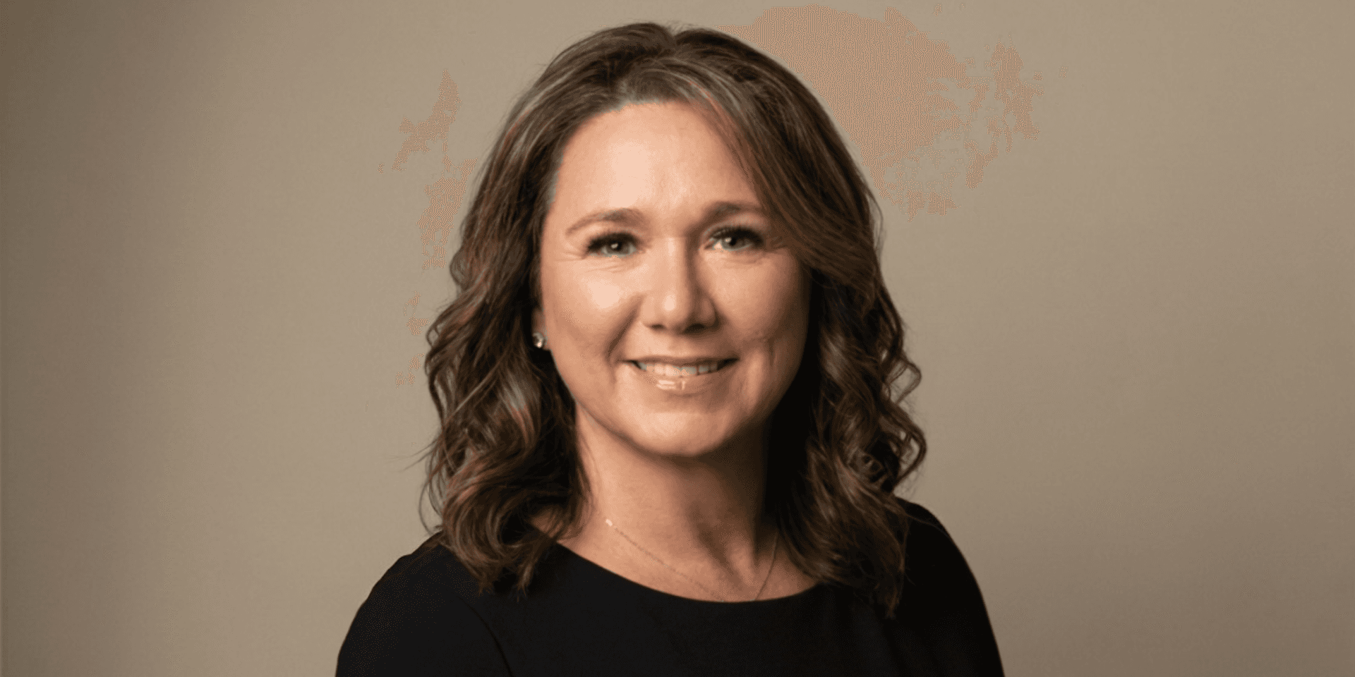Woman with wavy brown hair smiling against a neutral background