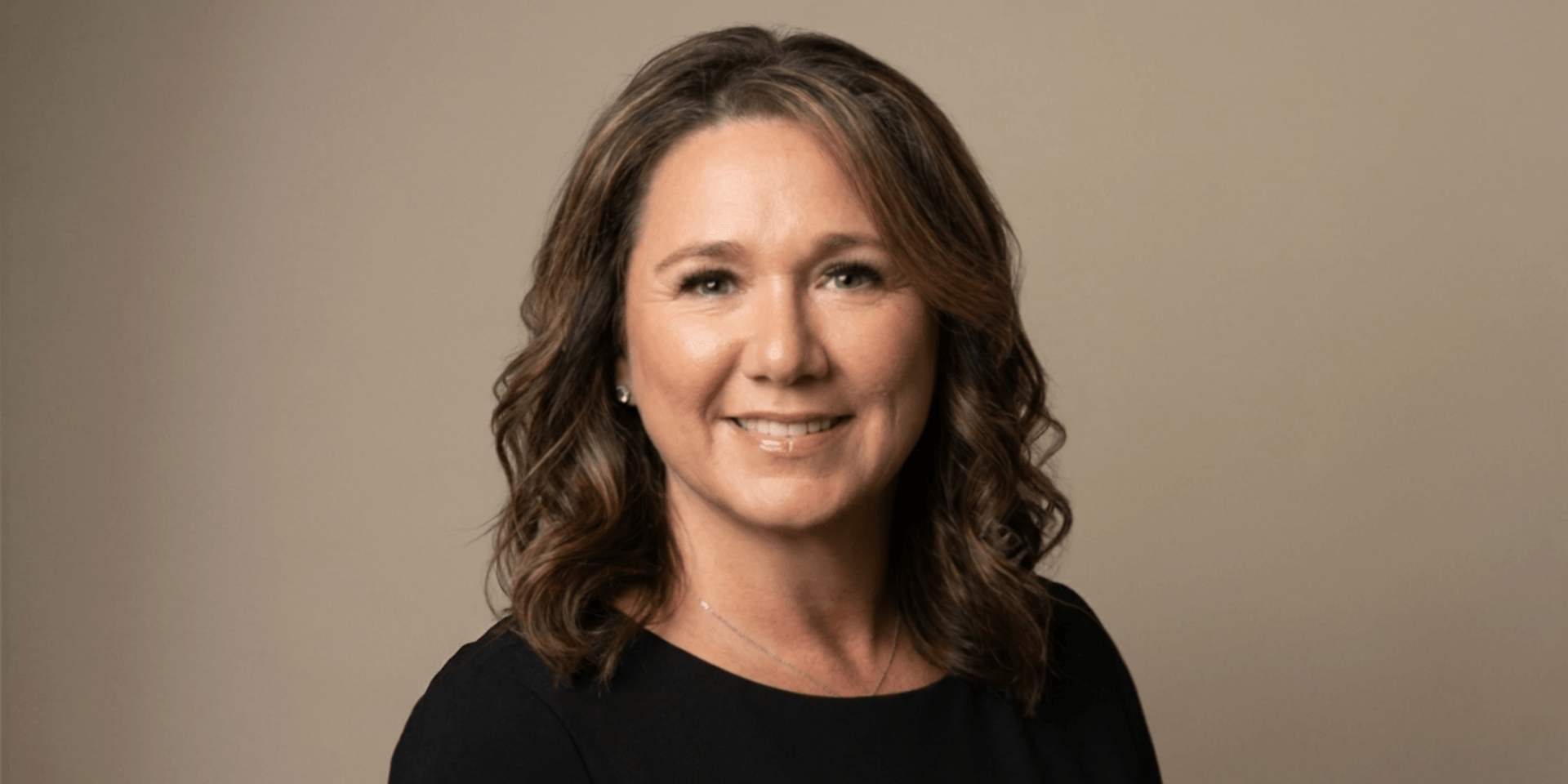 Woman with wavy brown hair smiling against a neutral background