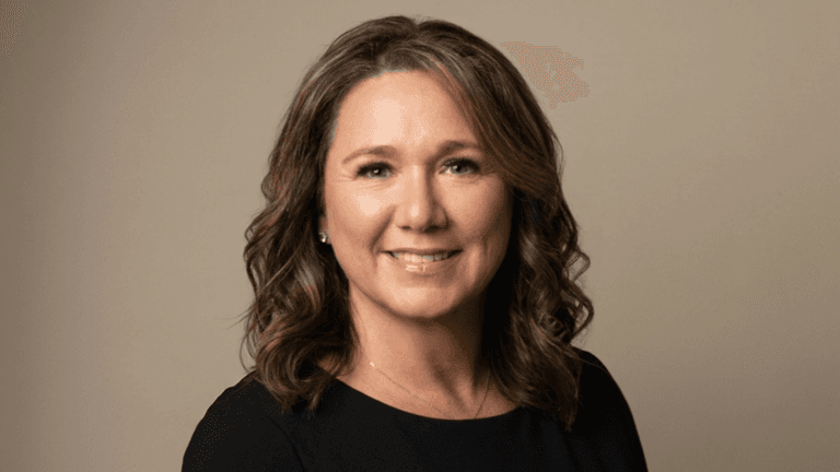 Woman with wavy brown hair smiling against a neutral background