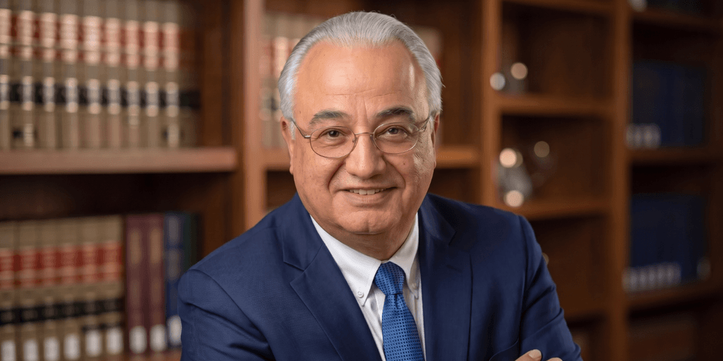 Smiling man in a blue suit poses in a library with law books behind.