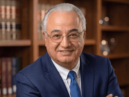 Smiling man in a blue suit poses in a library with law books behind.