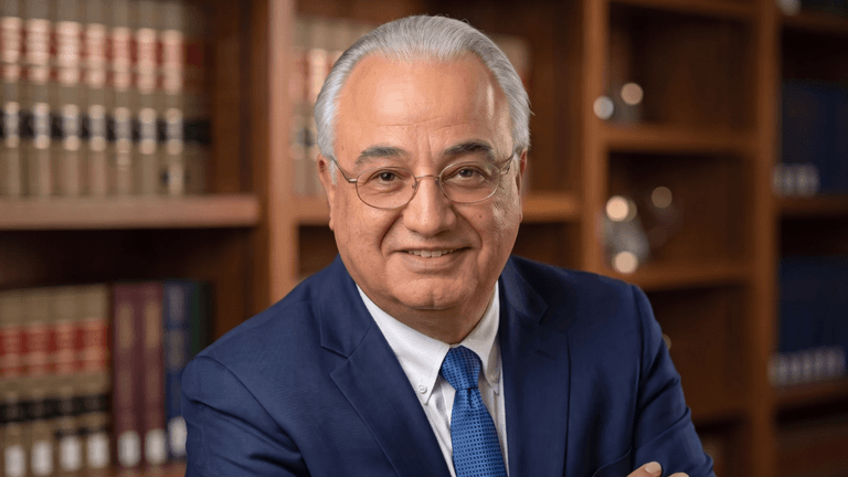 Smiling man in a blue suit poses in a library with law books behind.
