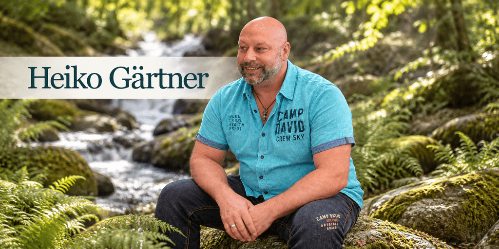 Man in a blue shirt sitting on mossy rocks by a stream in nature