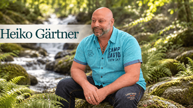 Man in a blue shirt sitting on mossy rocks by a stream in nature