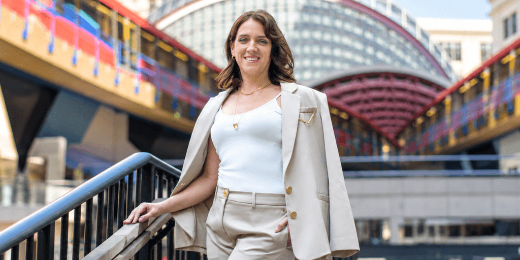 A woman in a beige suit stands confidently on an outdoor staircase.