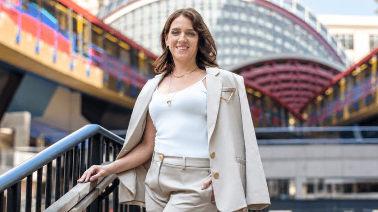 A woman in a beige suit stands confidently on an outdoor staircase.