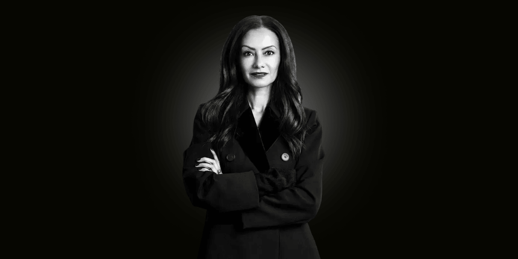 A woman in a dark coat stands confidently with her arms crossed against a black background