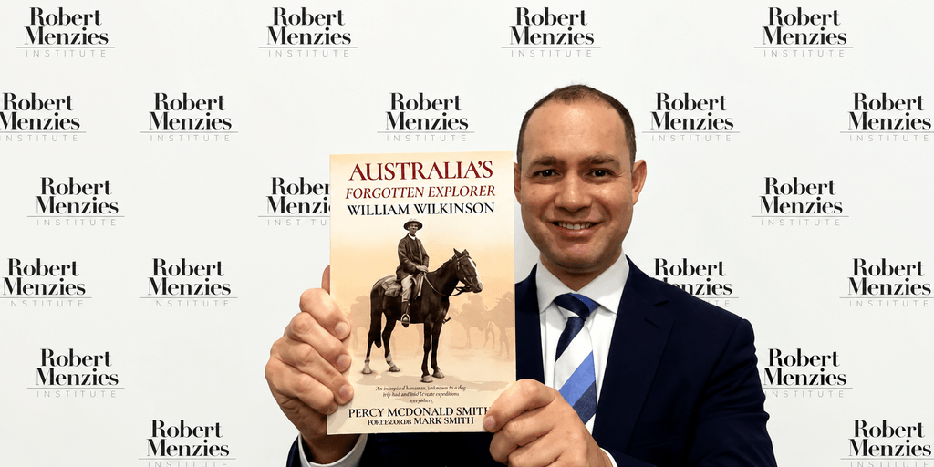 Man holding a book titled "Australia's Forgotten Explorer" in front of a backdrop.