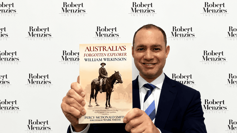 Man holding a book titled "Australia's Forgotten Explorer" in front of a backdrop.