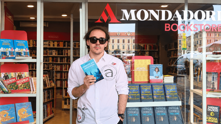 Man holding a book outside a Mondadori bookstore with book displays visible