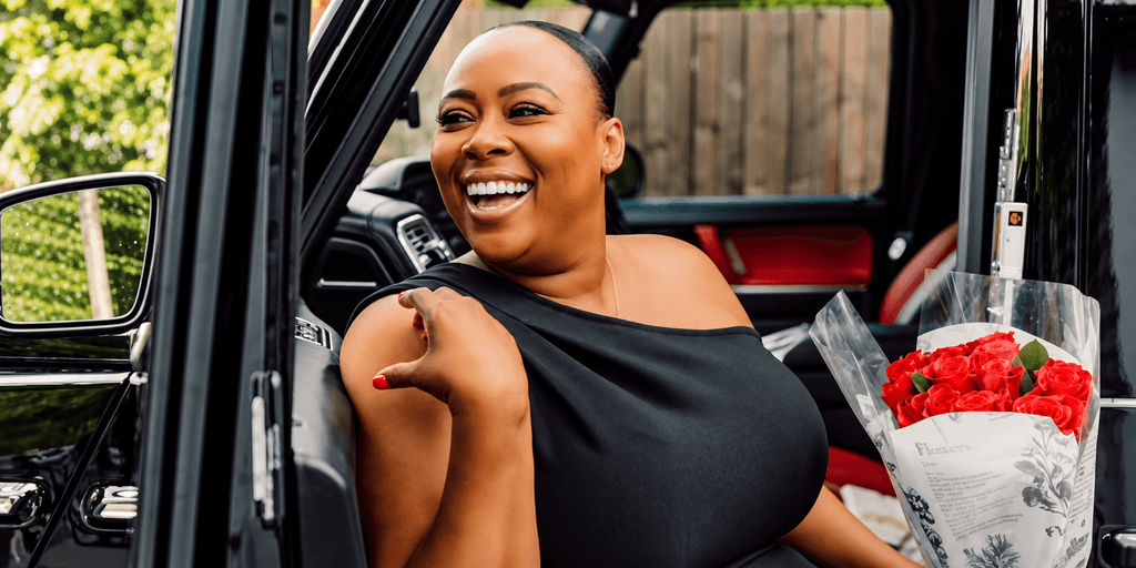 Smiling woman in black dress holds bouquet of red roses in car doorway
