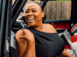 Smiling woman in black dress holds bouquet of red roses in car doorway