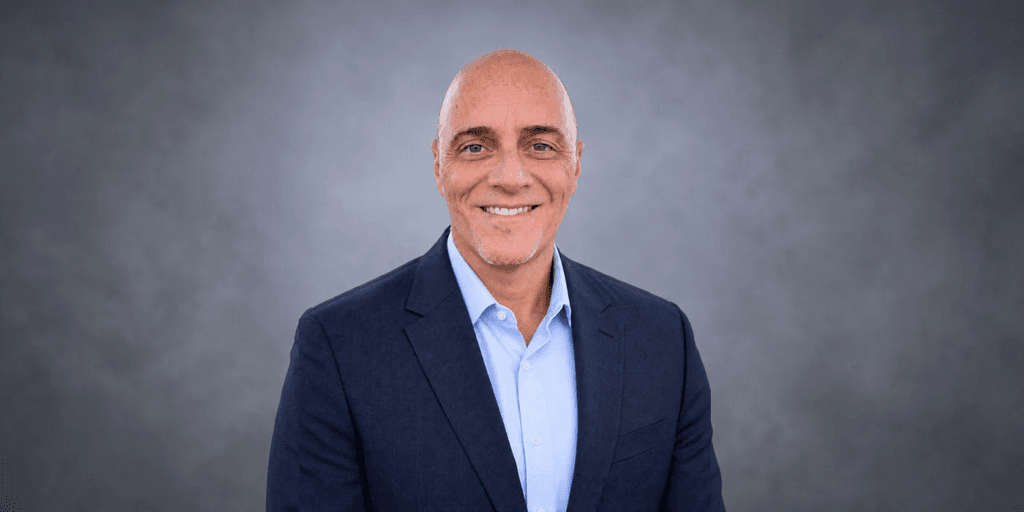 Smiling man in a blazer and shirt against a gray background