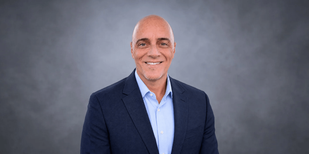Smiling man in a blazer and shirt against a gray background
