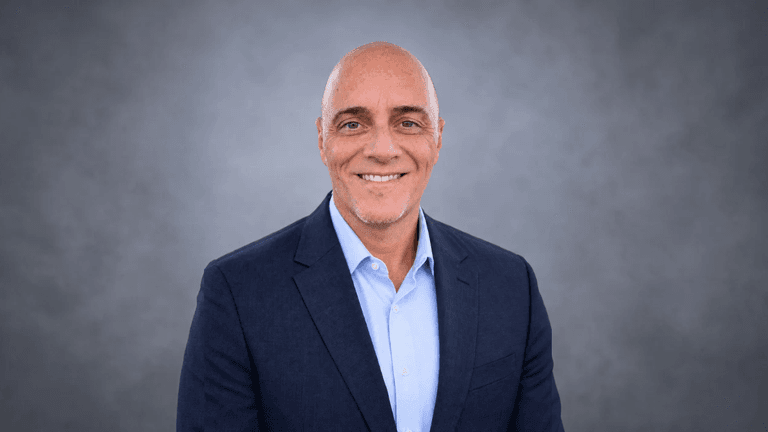 Smiling man in a blazer and shirt against a gray background
