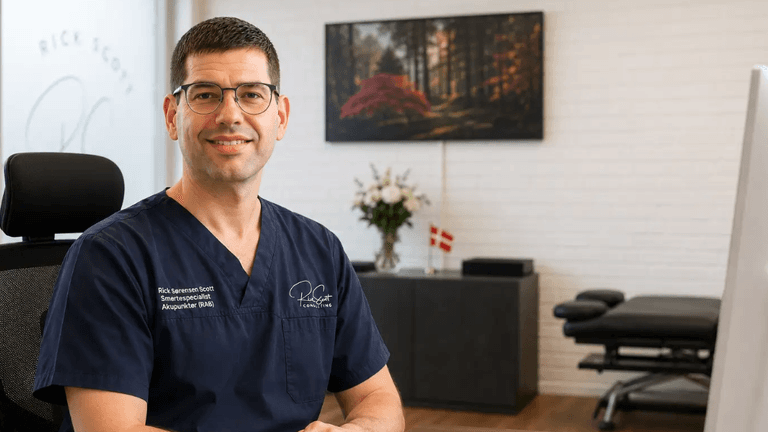 Male professional in scrubs smiling in a modern office setting with plants