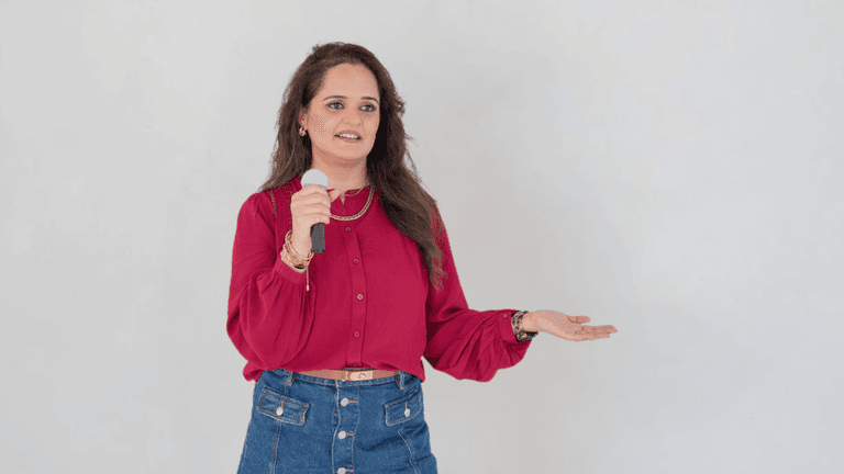 A woman in a red blouse holds a microphone while speaking or presenting