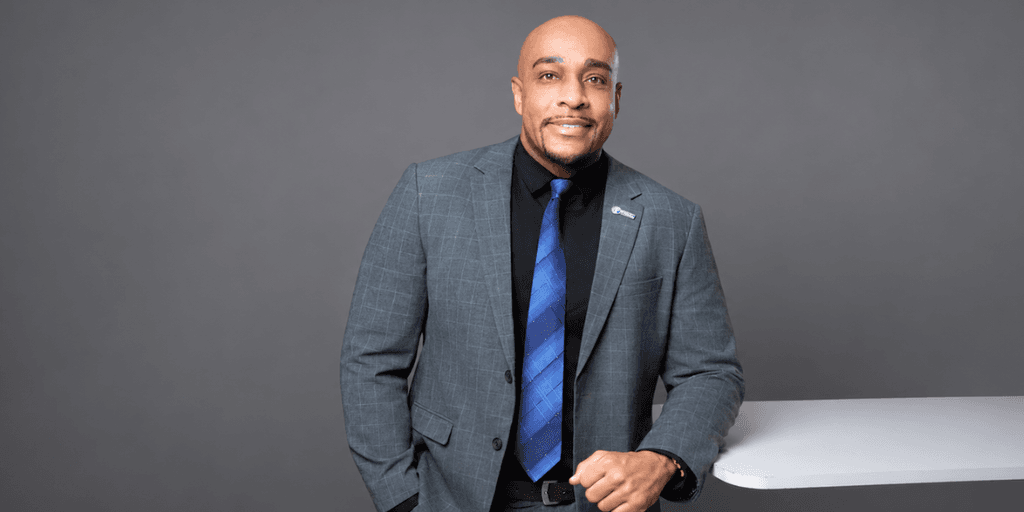 Man in a suit stands confidently beside a white table against a gray background