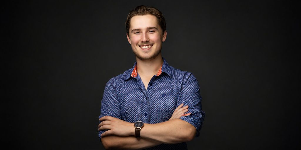 Professional portrait of Trystan Keller smiling with arms crossed against a dark background.