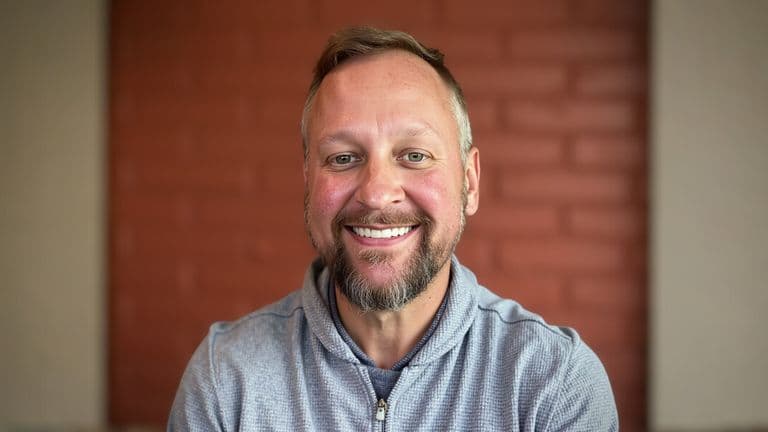 Mike Snellenberger, the founder of The Fractional CMO Team, smiling confidently with a brick wall background.