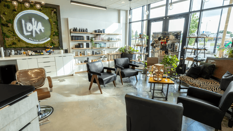 Modern beauty salon interior with sleek furniture, greenery, and a moss wall displaying 'LOKA Beauty Studio' logo.