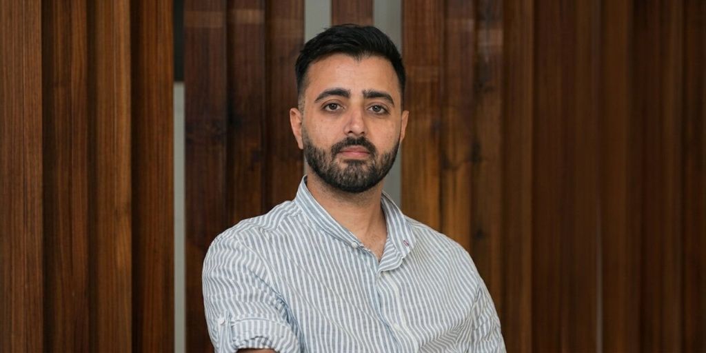 Portrait of entrepreneur Pourya Balali seated indoors against a wooden-paneled background.