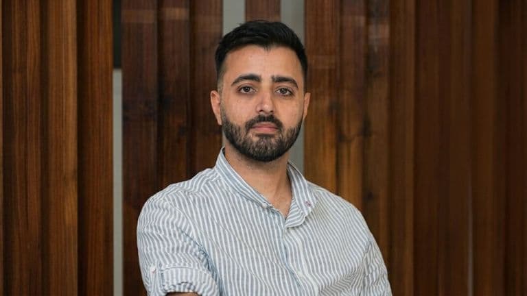 Portrait of entrepreneur Pourya Balali seated indoors against a wooden-paneled background.
