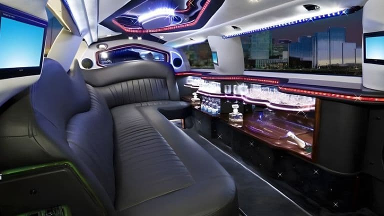 Interior of a luxury limousine with leather seating, ambient lighting, bar area, and modern entertainment system for special events.