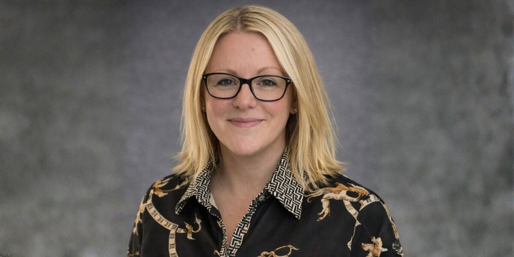 Hannah Hally, founder of The Business Book Club, wearing a patterned blouse, smiling confidently with a professional backdrop.