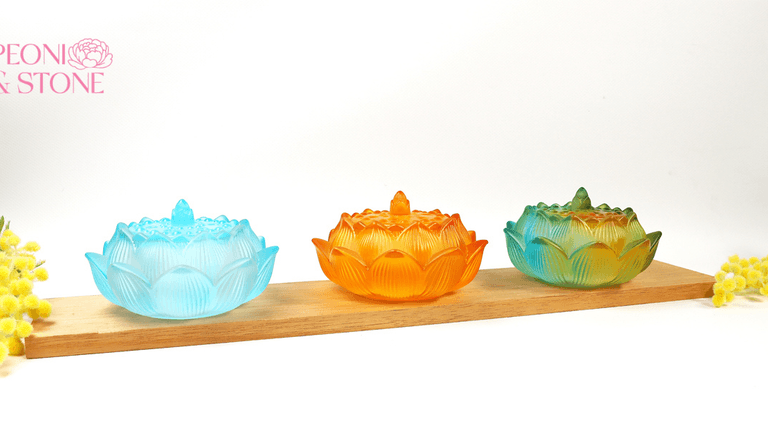 Colorful lotus-shaped incense burners displayed on a wooden shelf with flowers and Peoni & Stone branding.