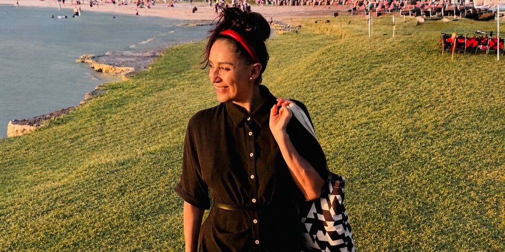 Daniela Jines walks along a waterfront at sunset, reflecting her people-centered approach to organizational happiness.