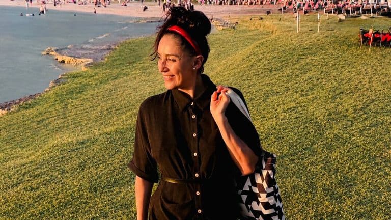 Daniela Jines walks along a waterfront at sunset, reflecting her people-centered approach to organizational happiness.
