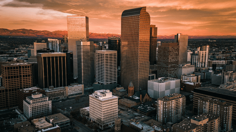 Downtown Denver skyline at sunset with modern skyscrapers and Rocky Mountains in the background
