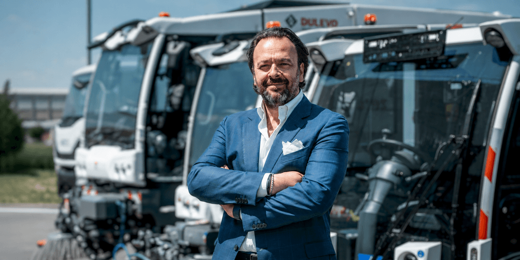 Umberto Maria Cini standing before Dulevo street sweepers at the company's manufacturing facility in Italy.