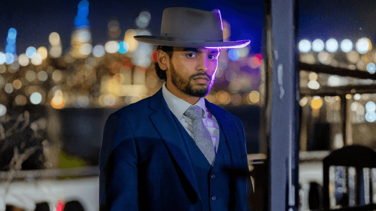 Isaiah Edward in a sharp suit and hat, standing confidently against a blurred cityscape, embodying professionalism and vision.