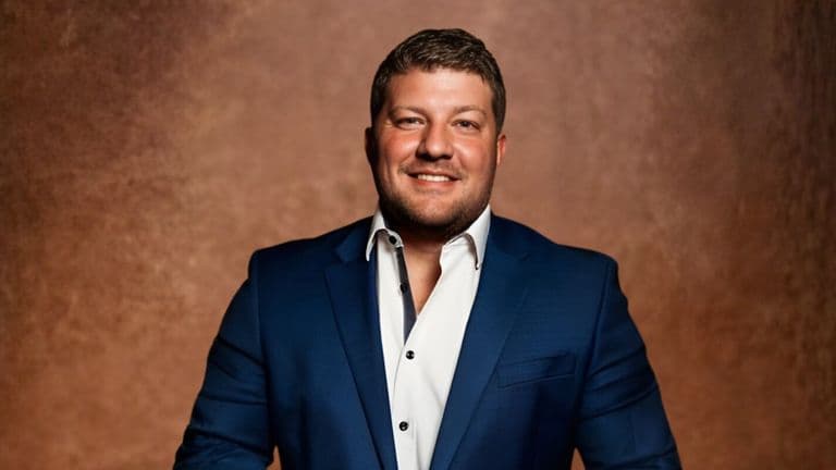 A man in a blue suit and white shirt stands confidently, representing professionalism in the real estate industry.