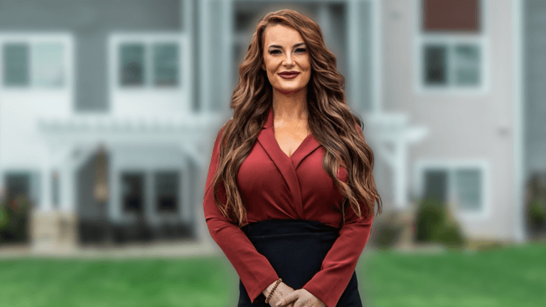 Alexis Anderson stands confidently outside a modern building, showcasing professionalism with her vibrant auburn hair and red attire.