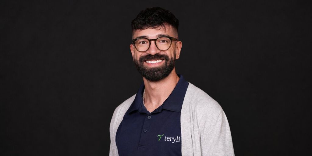 Christopher Molina wearing a Teryli polo shirt and smiling against a black studio background.