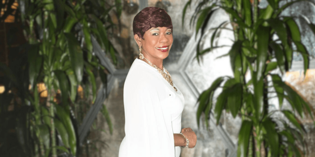 Dr. Patricia Rogers, a Visibility Strategist, smiling in a white gown with plants in the background.