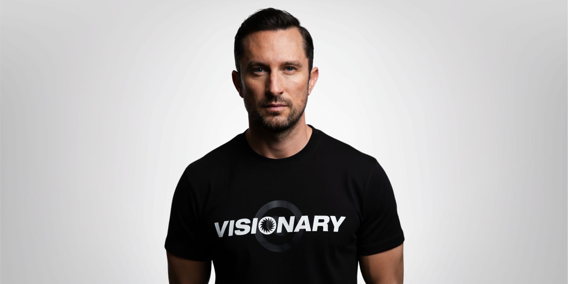 A man in a black "VISIONARY" t-shirt standing against a neutral background.
